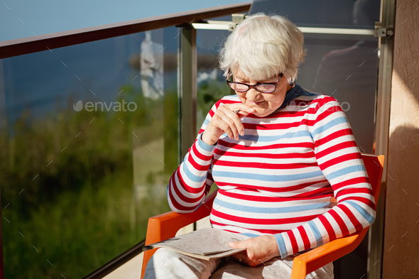 Elderly woman in glasses sitting on balcony near the sea