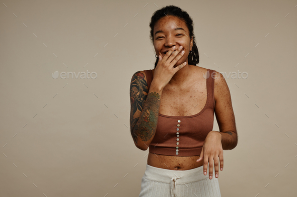 Candid ethnic young woman with tattoos laughing and covering face