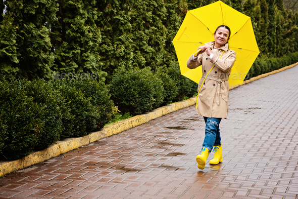 Happy senior woman in yellow rain coat with yellow umbrella Encouraging self-care and relaxation - Stock Photo - Images