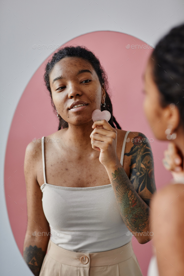 Young black woman with acne scars using face massager during beauty routine Stock Photo by