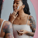 Candid young black woman with acne scars using face cream by mirror - PhotoDune Item for Sale