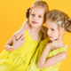 Twins girls are sitting on a chair on a yellow background. - PhotoDune Item for Sale