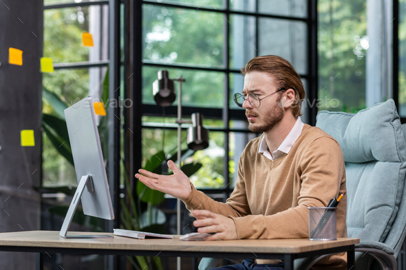 Frustrated and upset businessman reading news online from computer monitor, young blond man sad at
