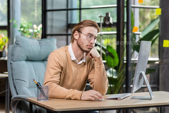 Frustrated and upset businessman reading news online from computer monitor, young blond man sad at