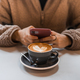 Girl in fluffy sweater holds a smartphone in hands, writes message next to cup of coffee with heart - PhotoDune Item for Sale