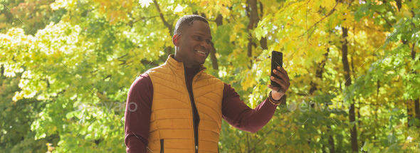 Banner african American man taking a self portrait with a smartphone in autumn fall park copy space - Stock Photo - Images