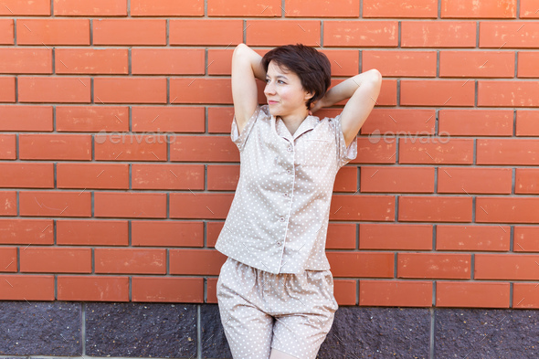 Cheerful woman in home wear pajama outdoor brick wall background emotions copy space and empty place - Stock Photo - Images