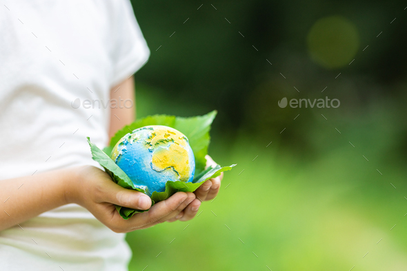 Kid holding small planet in hands against spring or summer green background. Ecology, environment - Stock Photo - Images