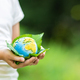 Kid holding small planet in hands against spring or summer green background. Ecology, environment - PhotoDune Item for Sale