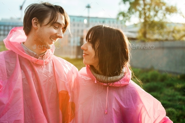 Closeup shot of a male and a female in pink plastic raincoats looking at each other romantically