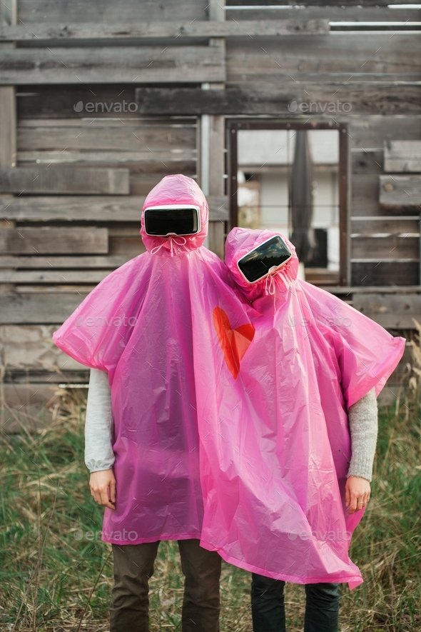 Vertical shot of two people in VR headsets sharing a pink plastic raincoat