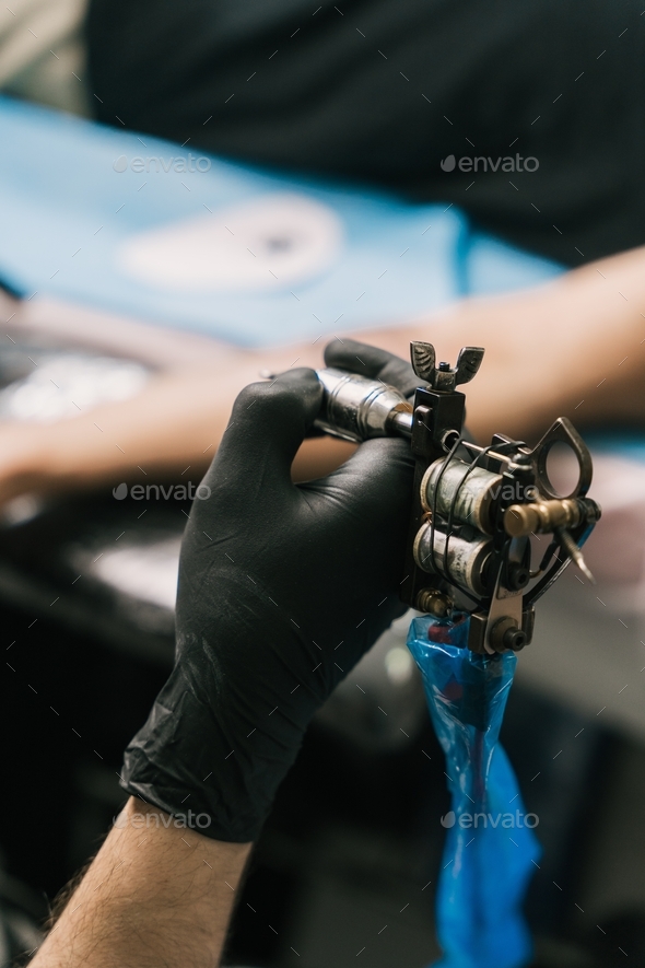 Selective focus shot of the hand of a tattoo artist wearing a black glove and holding a tattoo gun