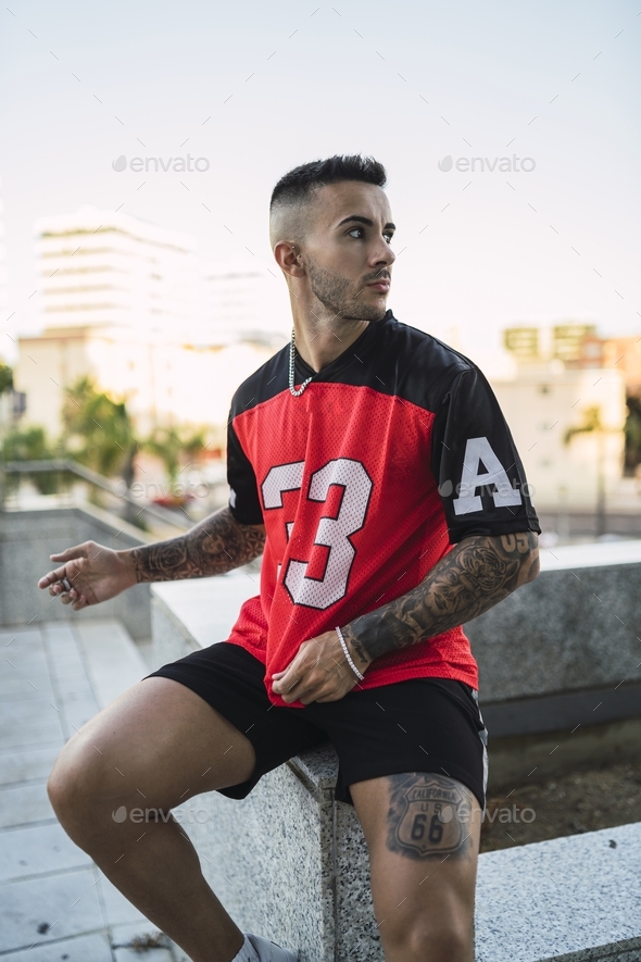 European tattooed hip male in a sporty outfit with red and black shorts and shirt
