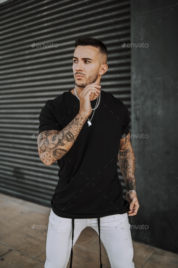 European tattooed hip male in a black shirt and white ripped jeans, and metal chain