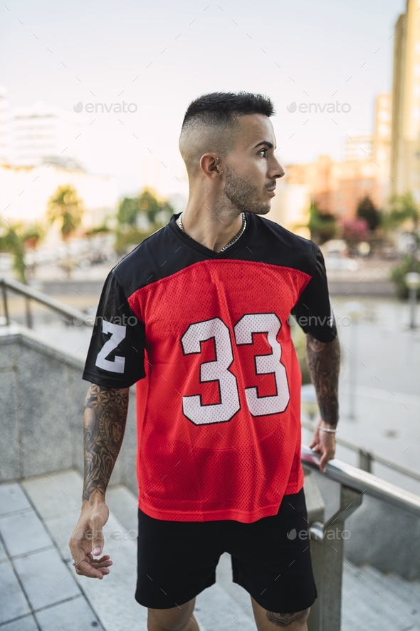 European hip male in a sporty outfit with red and black shorts and shirt, tattoos, and metal chain