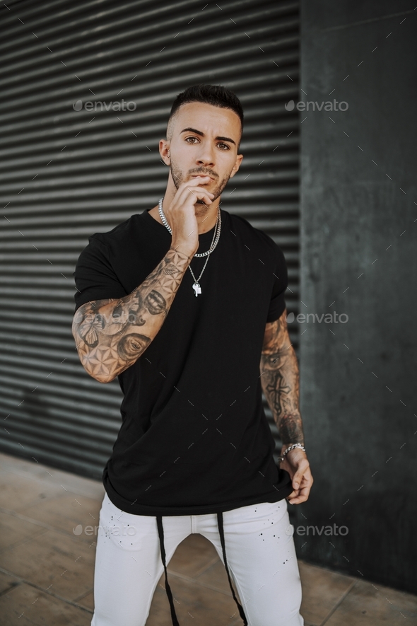European tattooed hip male in a black shirt and white ripped jeans, and metal chain