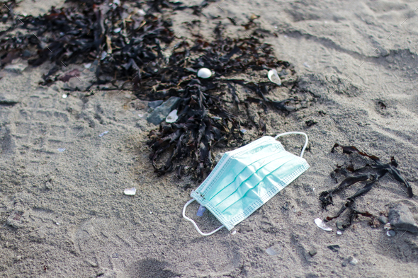 Closeup shot of a medical mask on a beach - Coronavirus waste polluting nature concept