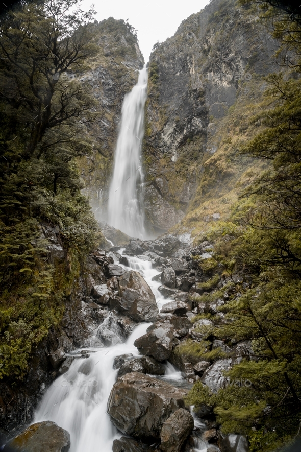 Vertical picture of Devils Punchbowl Waterfall surrounded by greenery in New Zealand - Stock Photo - Images