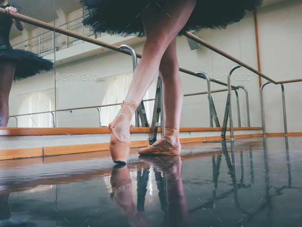 Ballerina in ballet pointe shoes stretches on barre. Woman