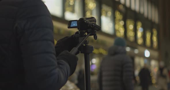 Photographer adjusts a camera on a tripod to capture a central city street at night. alt