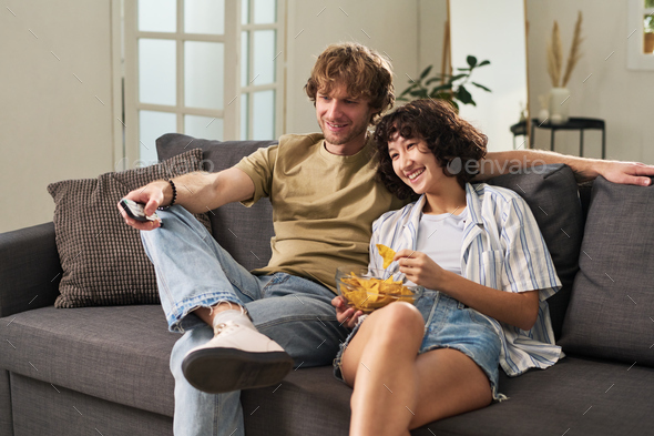 Young man with remote control choosing channel while sitting next to wife - Stock Photo - Images