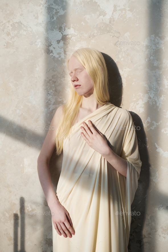 Serene albino girl in white attire standing by wall and enjoying sunlight - Stock Photo - Images