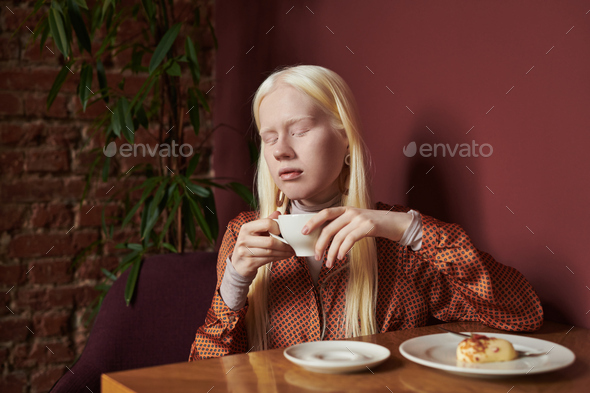 Young serene albino woman with long white hair holding cup of coffee - Stock Photo - Images