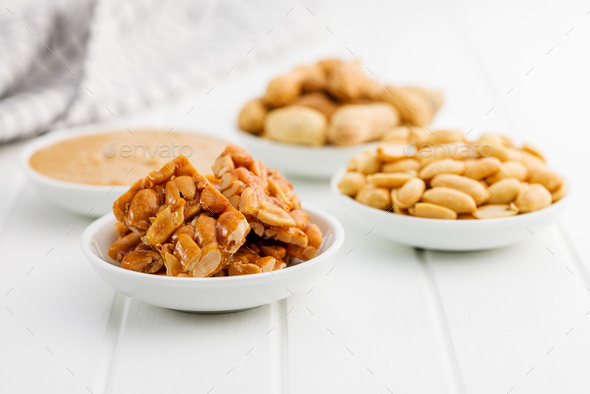 Sweet peanut brittle, peanuts and peanuts butter on white table.