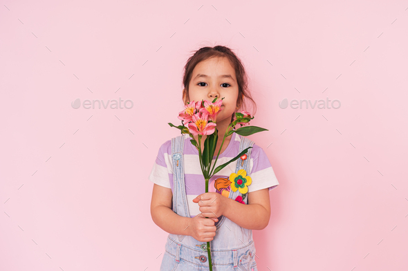 Little multi ethnic girl holding flowers against pink background, mother's day - Stock Photo - Images