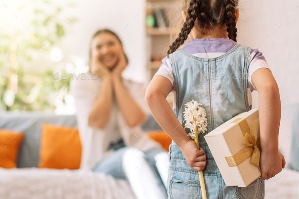 Child holding a gift and flowers behind her back in front of her mother, mother's day - Stock Photo - Images