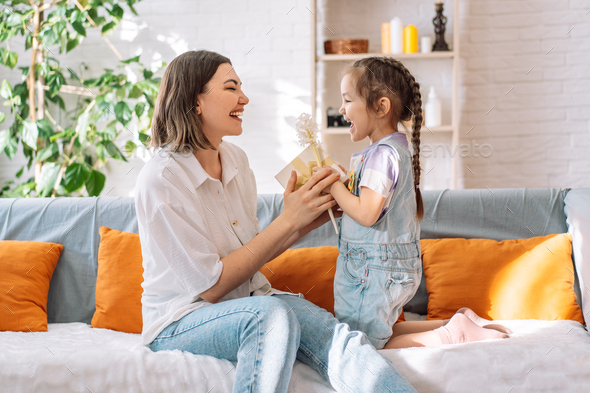 Daughter kissed her mother and gave gift with flowers while sitting on the sofa, mother's day - Stock Photo - Images