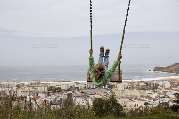 Little girl swinging against the scene of Nazare coast in Portugal - Stock Photo - Images