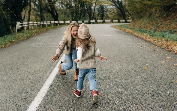 Mom is waiting in her arms for a little daughter running towards her on a walk along a rural road. - Stock Photo - Images