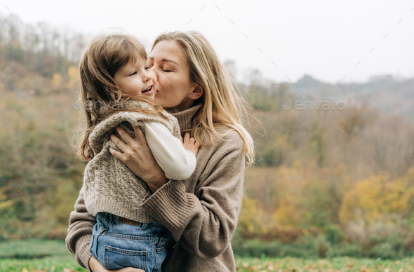 Mom kisses a little charming daughter, holding in her arms. - Stock Photo - Images
