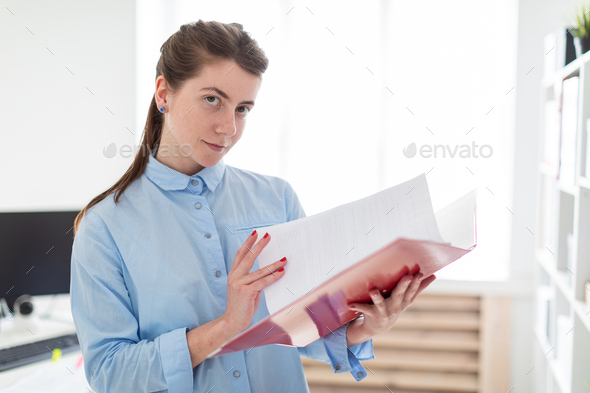 A young girl in the office is standing near the shelter and scrolls through the folder with the