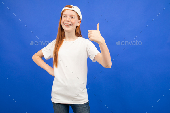 charming red-haired teenager girl in a white T-shirt with a layout shows a super class thumbs up on