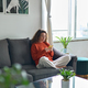 Young woman using mobile cell phone sitting on couch in living room. - PhotoDune Item for Sale
