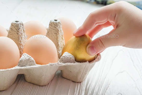 The child takes out a golden egg from the egg tray. A dozen chicken eggs on the table. Rise in price