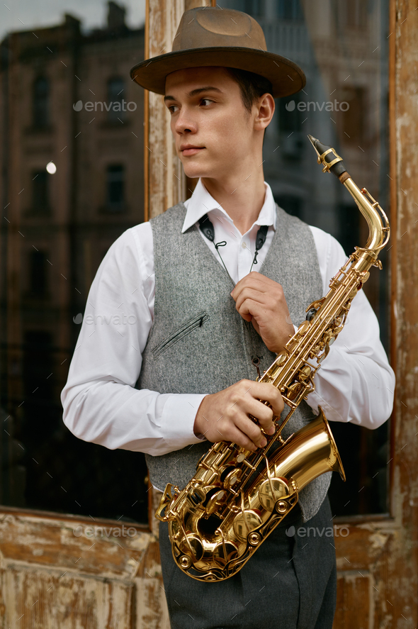 Young man holding saxophone standing on balcony terrace