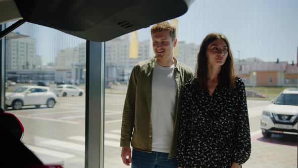 The Manager of the Dealership Shows the Young Couple the New Functions of the Car alt