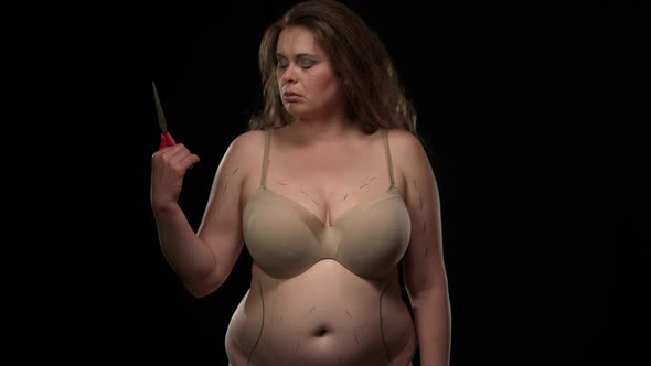 Portrait of Sad Caucasian Overweight Woman with Plastic Operation Markings Raising Scissors alt