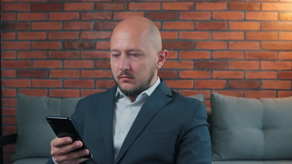Bald young man in the suit using a smartphone in a hand, indoors
