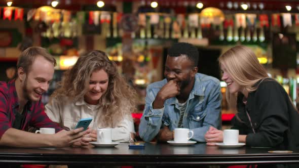 African-American Man with a Girl Looking at a Smartphone and Talking While Sitting in a Coffee and alt