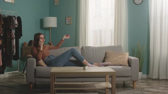 Young Woman with Red Apple Lies on Sofa and Talks on Phone