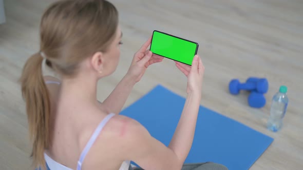 Rear View of Young Woman Looking at Smartphone with Chroma Key Screen on Yoga Mat alt