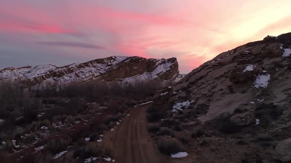 Flying over dirt road and rising above the landscape viewing colorful sunset alt