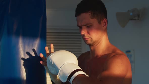 Attractive Young Man Puts on White Boxing Gloves to Practice Box on Punching Bag Onboard Ship
