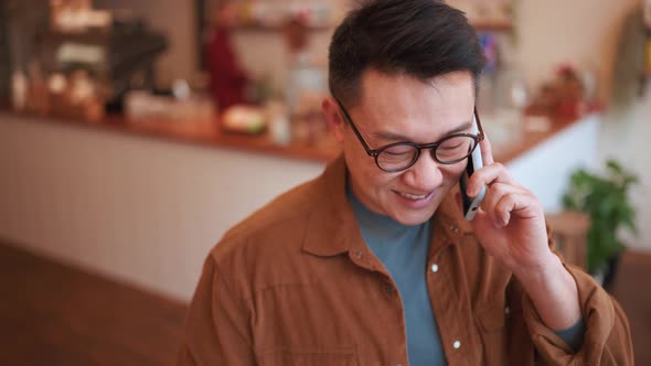 Laughing Asian young man wearing eyeglasses talking on phone alt