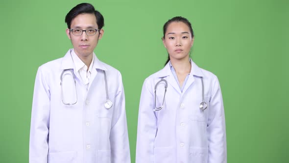 Young Asian Couple Doctors Pointing Up Together