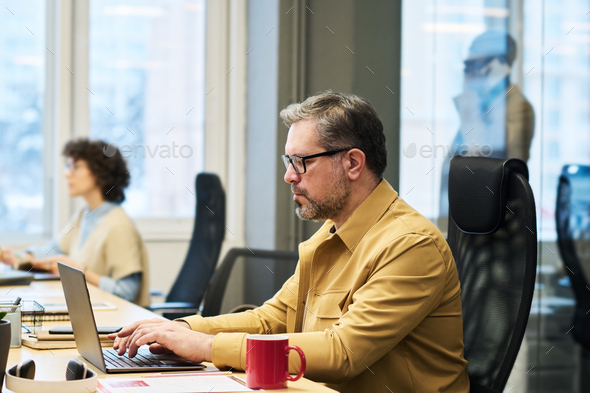 Side view of experienced manager typing on laptop keypad by workplace - Stock Photo - Images